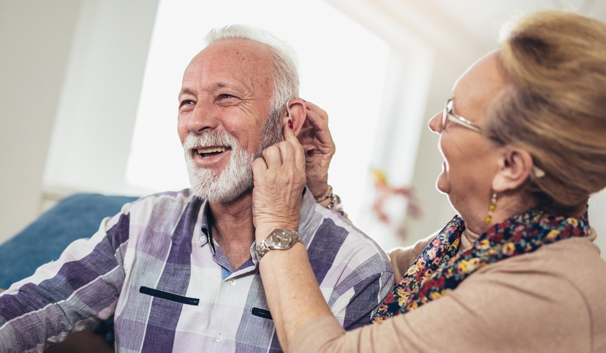 Frau hilft ihrem lachenden Partner beim Einsetzen des Hoergeraets