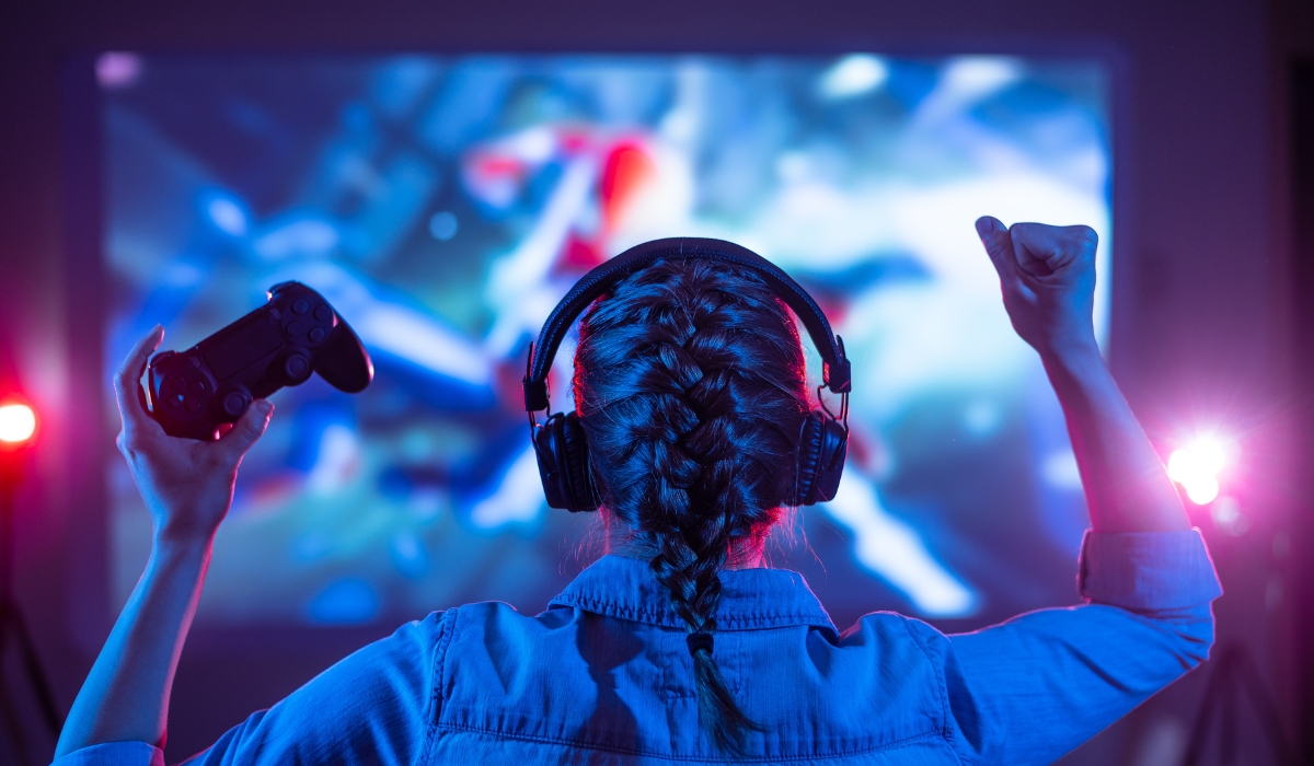 Frau-mit-Kopfhoerern-und-geflochtenem-Haar-jubelt-mit-Gamecontroller-vor-grossem-Bildschirm-in-farbenfroher-Gaming-Umgebung Frau-mit-Kopfhoerern-und-geflochtenem-Haar-jubelt-mit-Gamecontroller-vor-grossem-Bildschirm-in-farbenfroher-Gaming-Umgebung