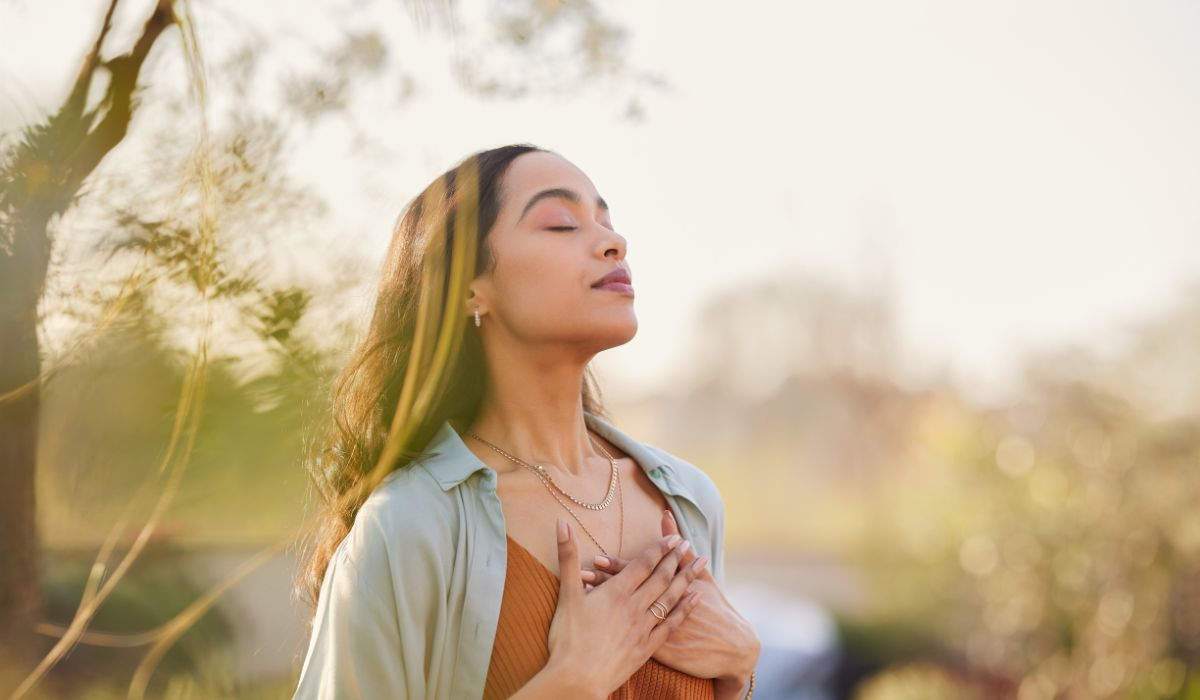 Frau steht entspannt im Freien und atmet tief durch