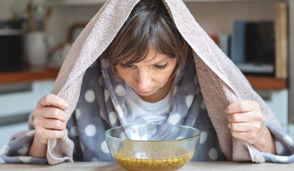Frau inhaliert über einer Schüssel mit heißem Kamillendampf