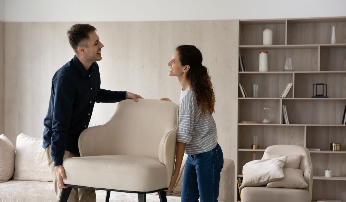 Junges Paar hebt gemeinsam einen Sessel im Wohnzimmer
