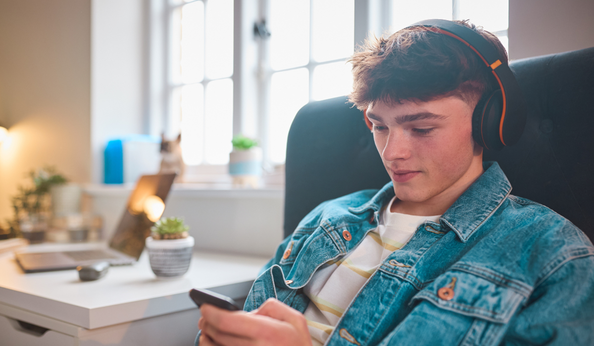 Jugendlicher mit Kopfhoerern nutzt entspannt sein Smartphone Jugendlicher mit Kopfhoerern nutzt entspannt sein Smartphone