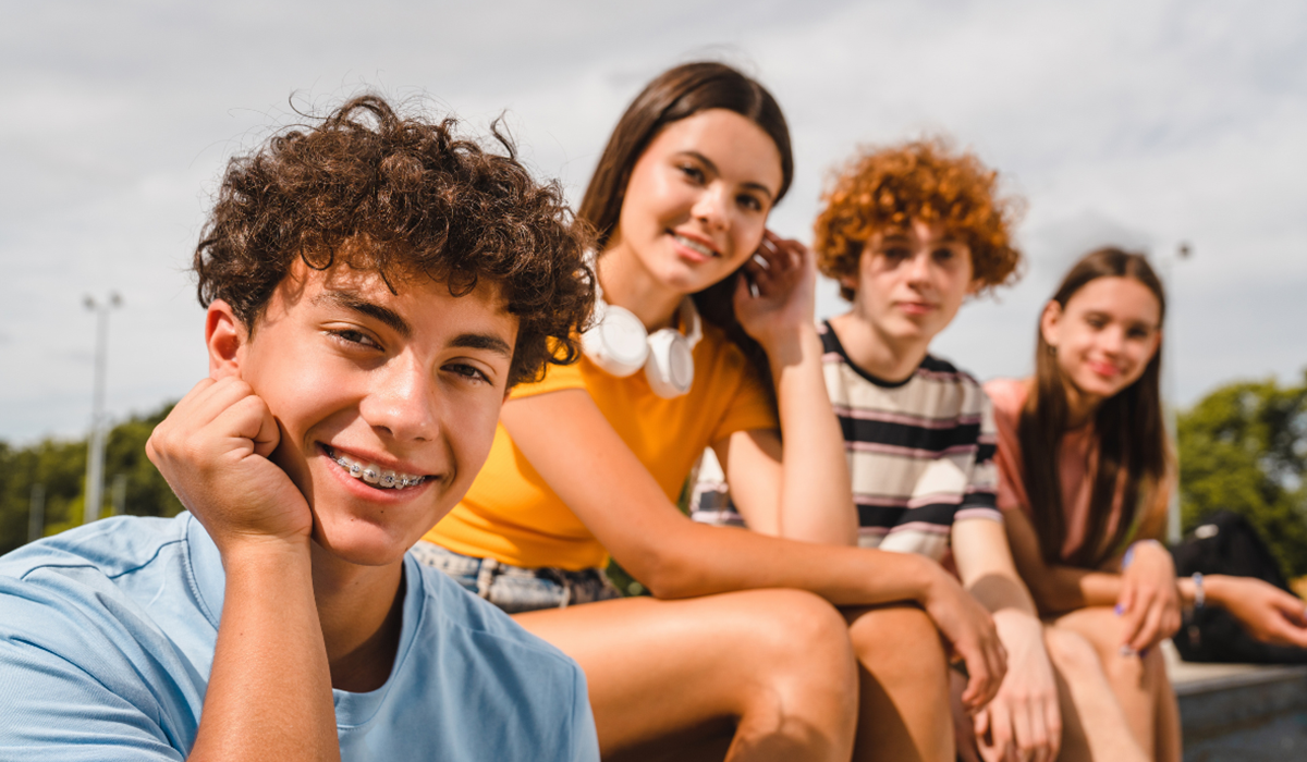 Vier Jugendliche sitzen gemeinsam draussen und laecheln in die Kamera